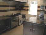 Main Kitchen with a range of stainless steel work tops and inset sinks, wash basin, microwave, fridge, grills, large commercial cooker, small cooker ten ring hob and large extractor fan.
